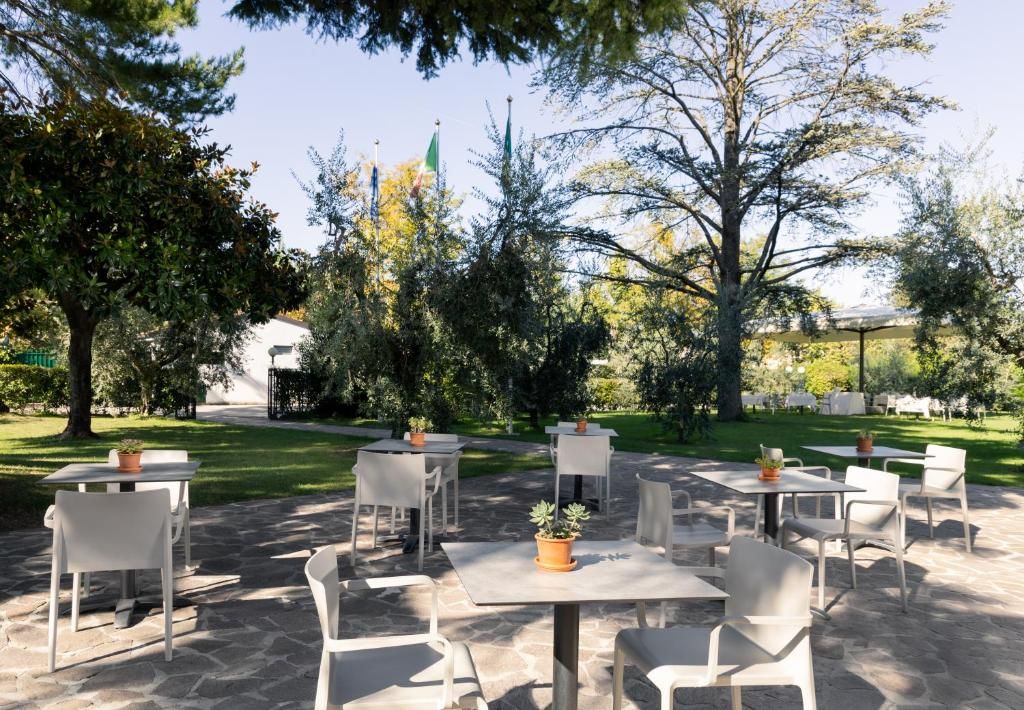 An outdoor patio area with tables and chairs, surrounded by trees and a stone pathway.
