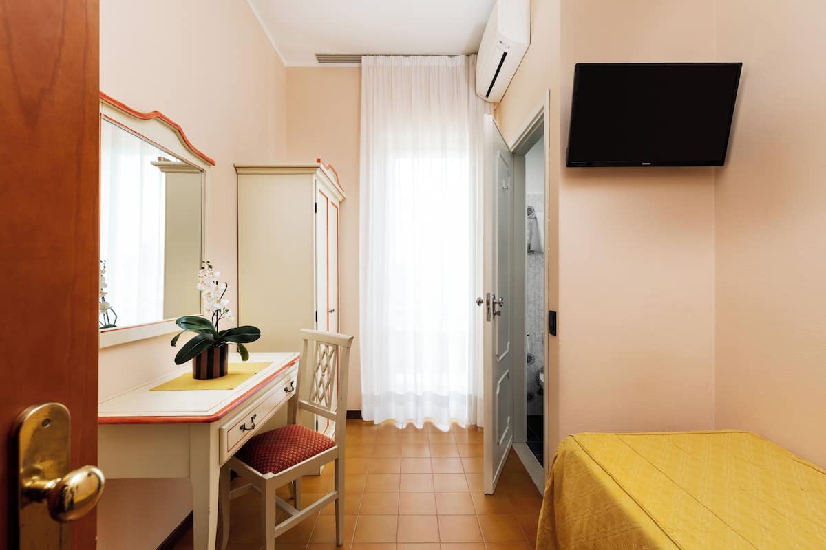 A hotel room with a desk, chair, potted plant, and a bed.