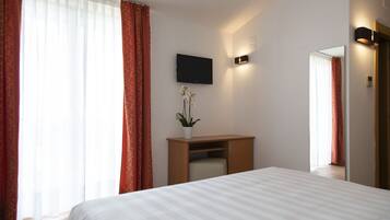 Ein Hotelzimmer mit Bett, Schreibtisch, Fernseher und einer Topfpflanze.