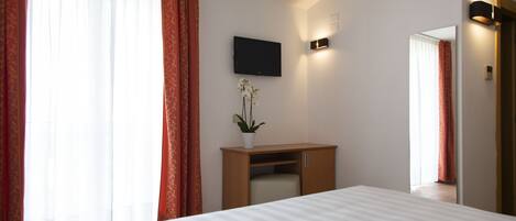 A hotel room with a bed, a desk, a TV, and a potted plant.