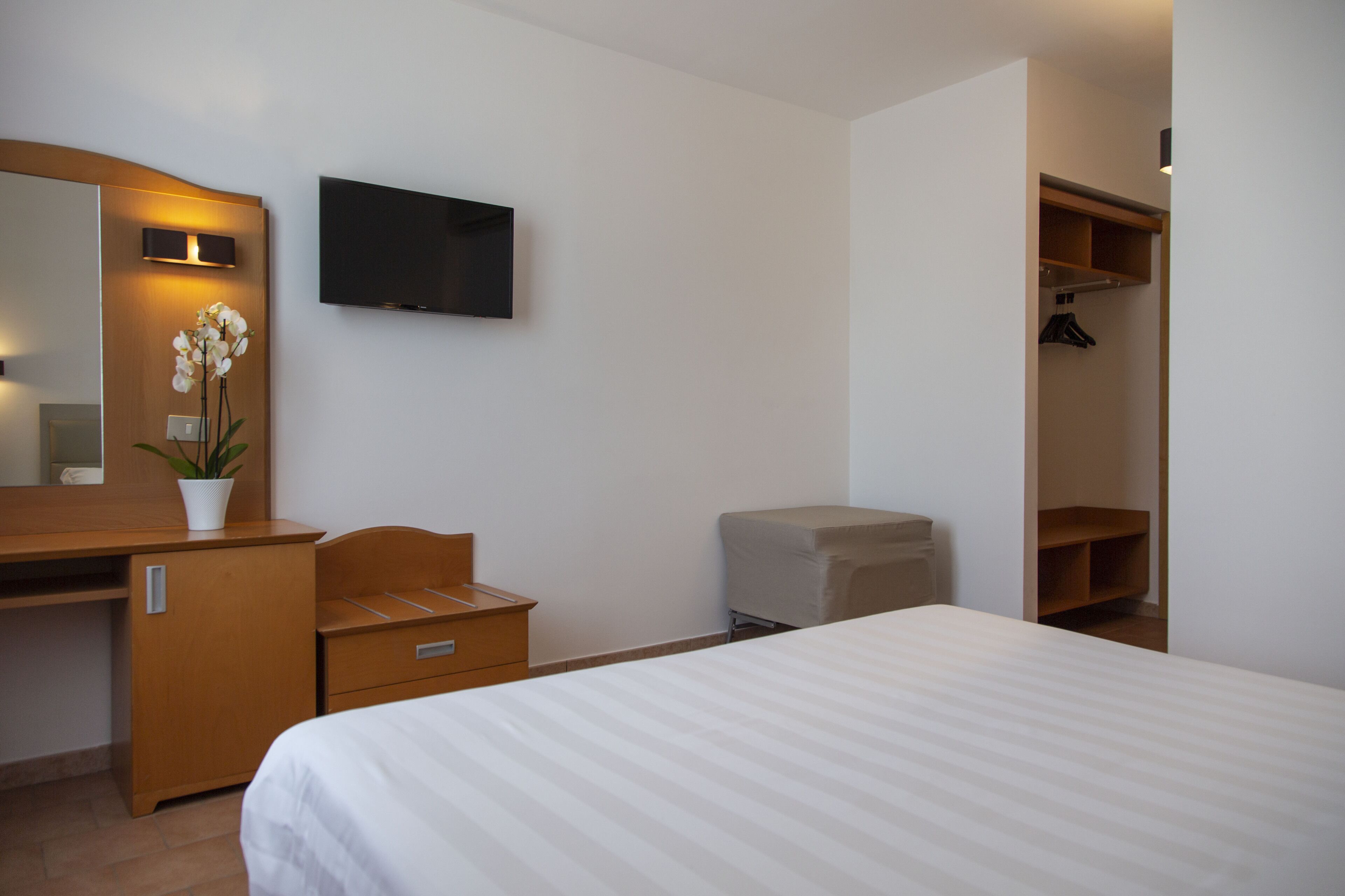 Une chambre d’hôtel comprenant un lit, un bureau en bois avec un miroir, une télévision et une armoire.