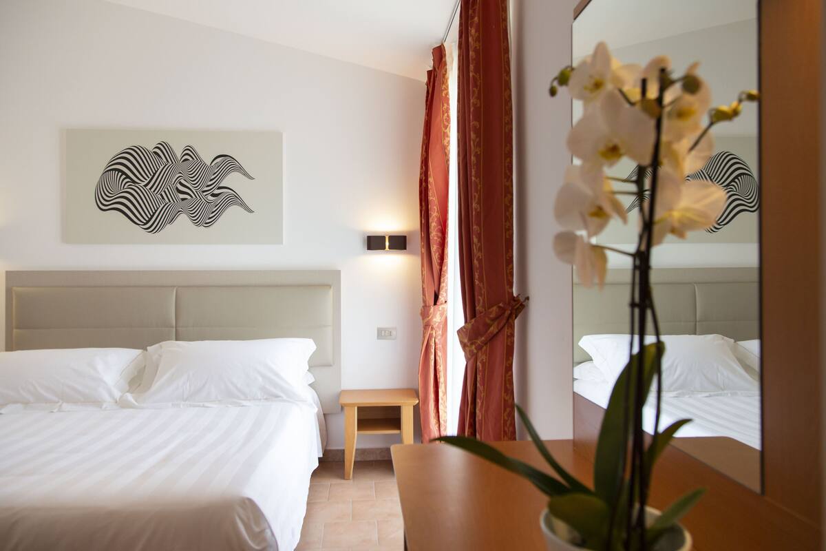 Ein Hotelzimmer mit Bett, Nachttisch, Spiegel und einem Wandbild.