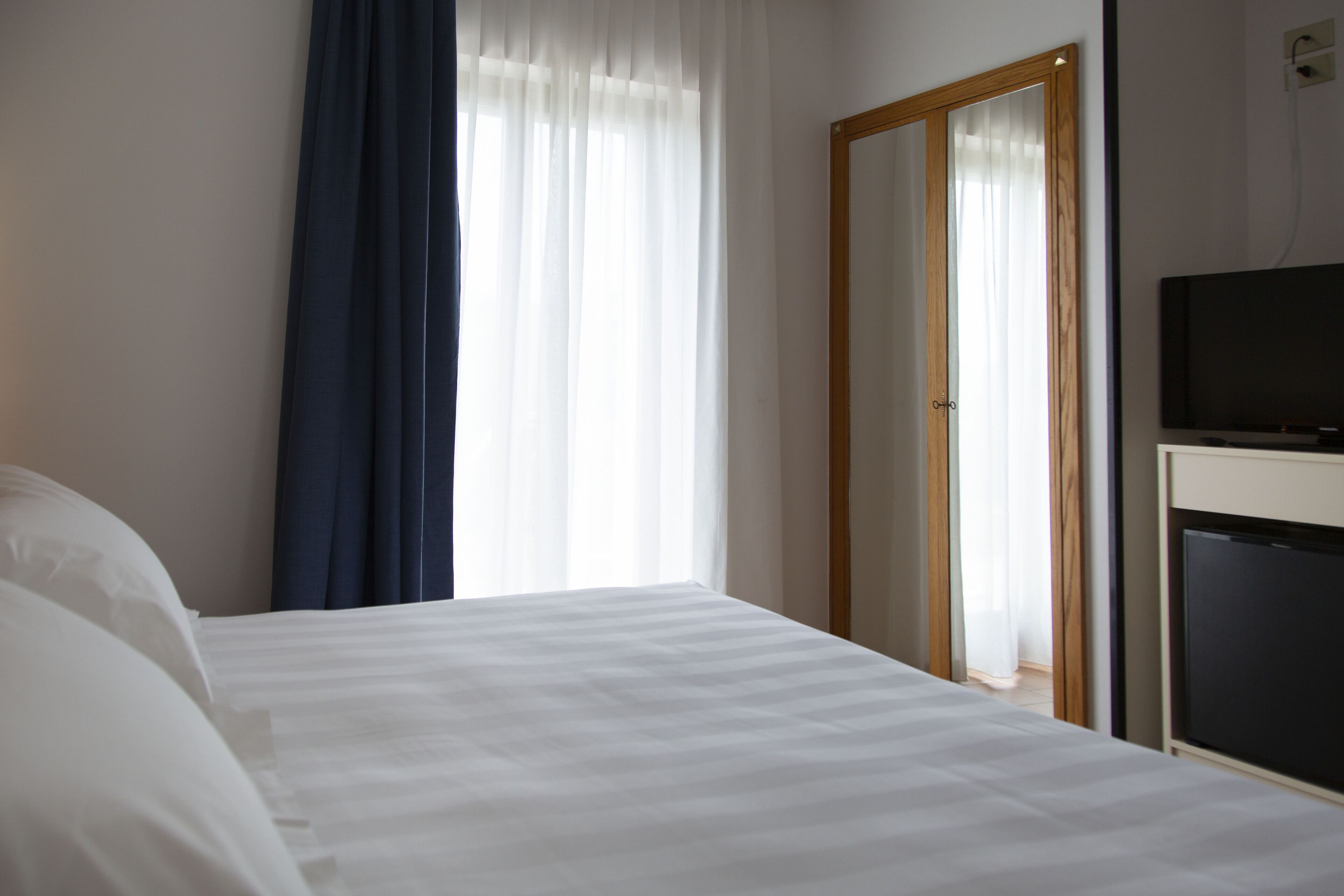 Una camera d'albergo con un letto, una televisione e un ingresso che dà su un'altra stanza.