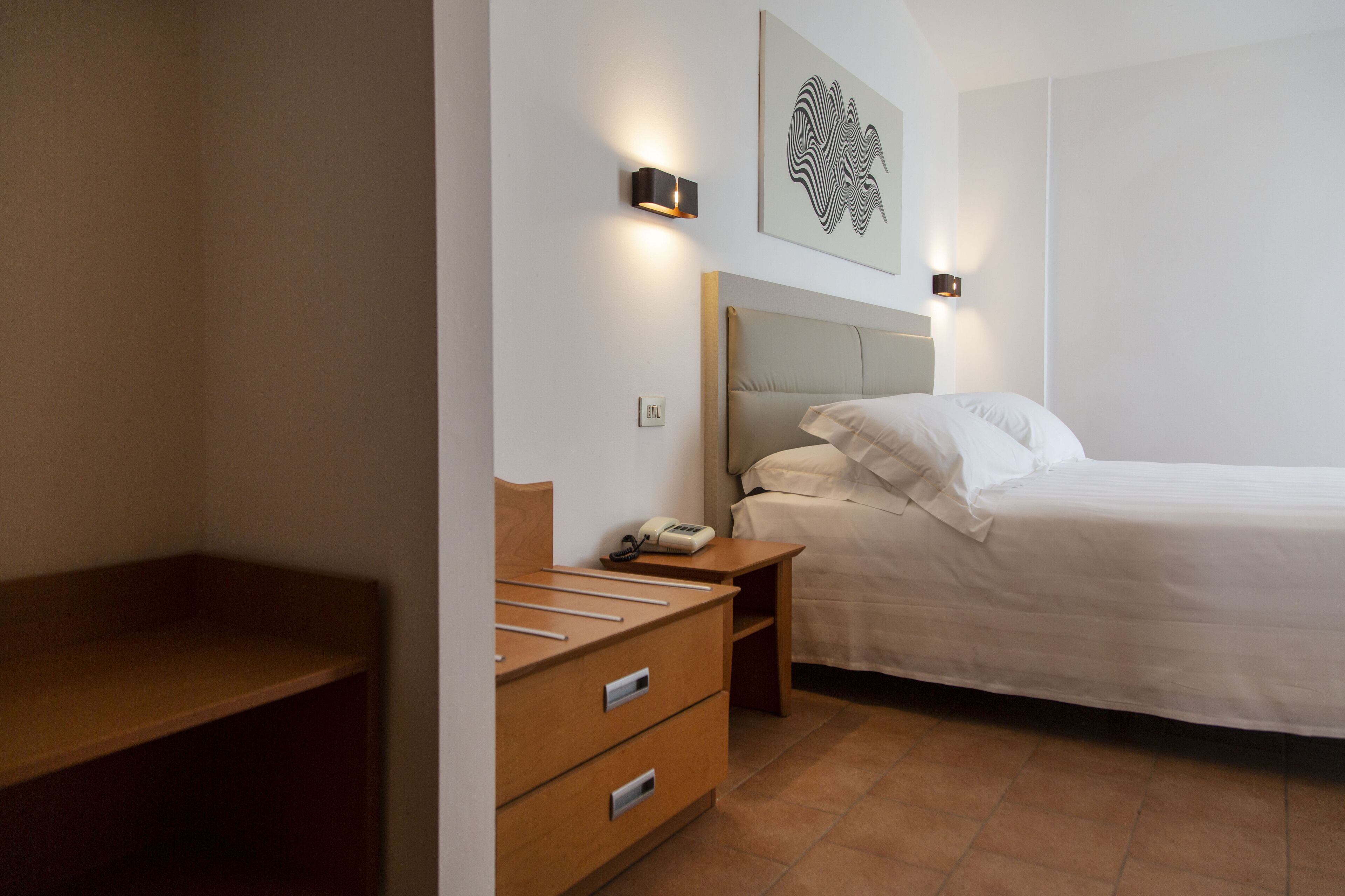 Een slaapkamer met een bed, houten nachtkastjes, een bureau en een wandlamp.