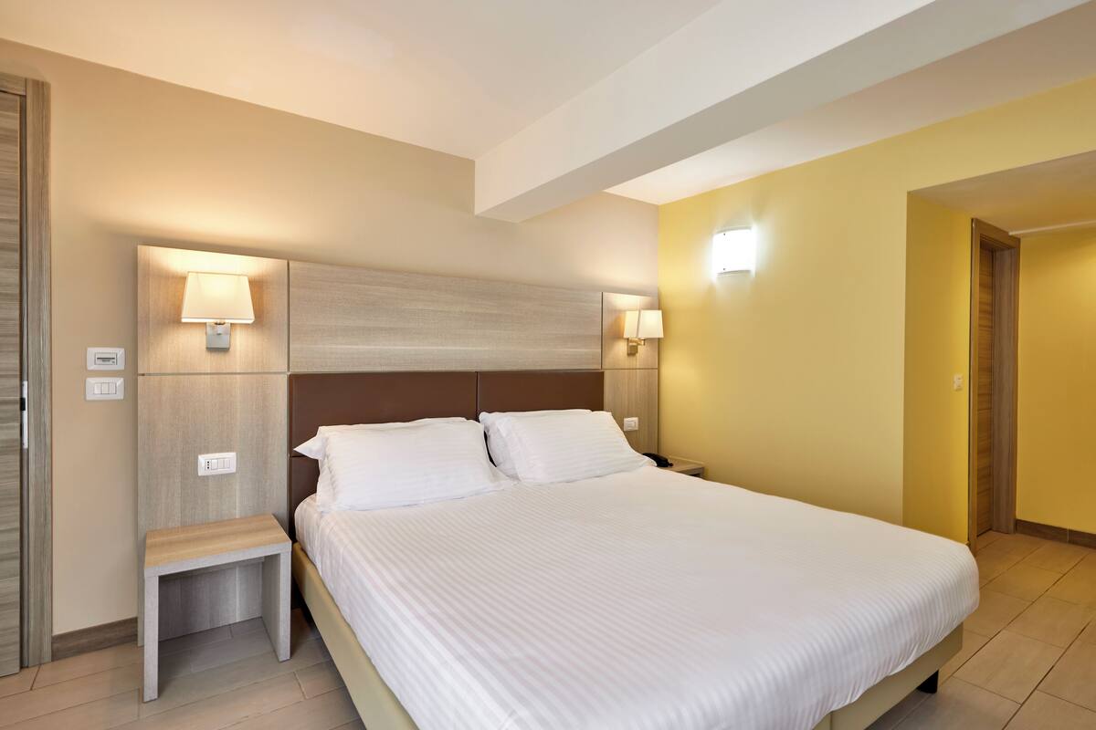 A hotel room with a large bed, two bedside tables, and wall-mounted lamps.