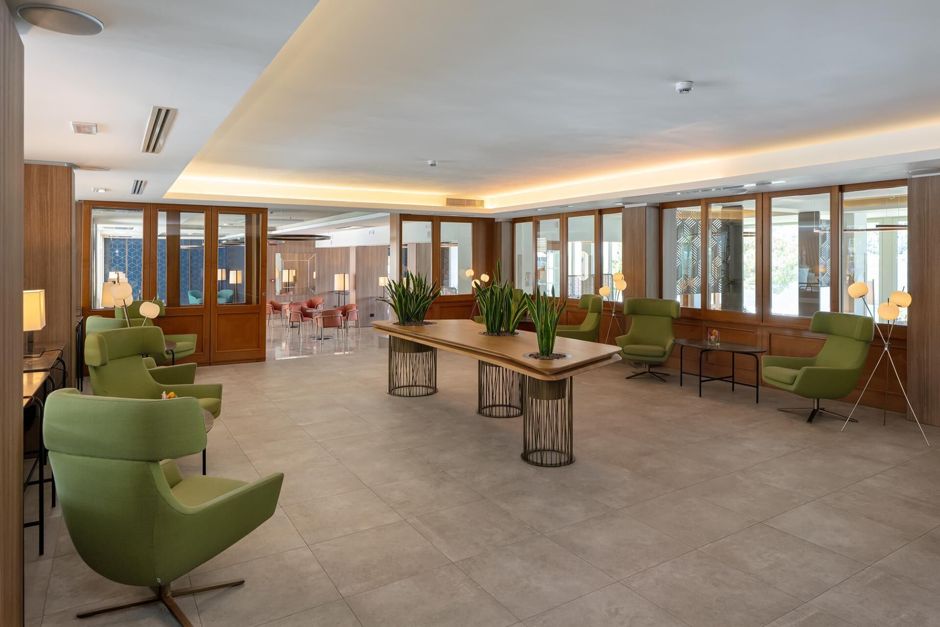 Un hall d’entrée spacieux, avec une longue table en bois, des chaises vertes et de grandes fenêtres offrant une vue dégagée.