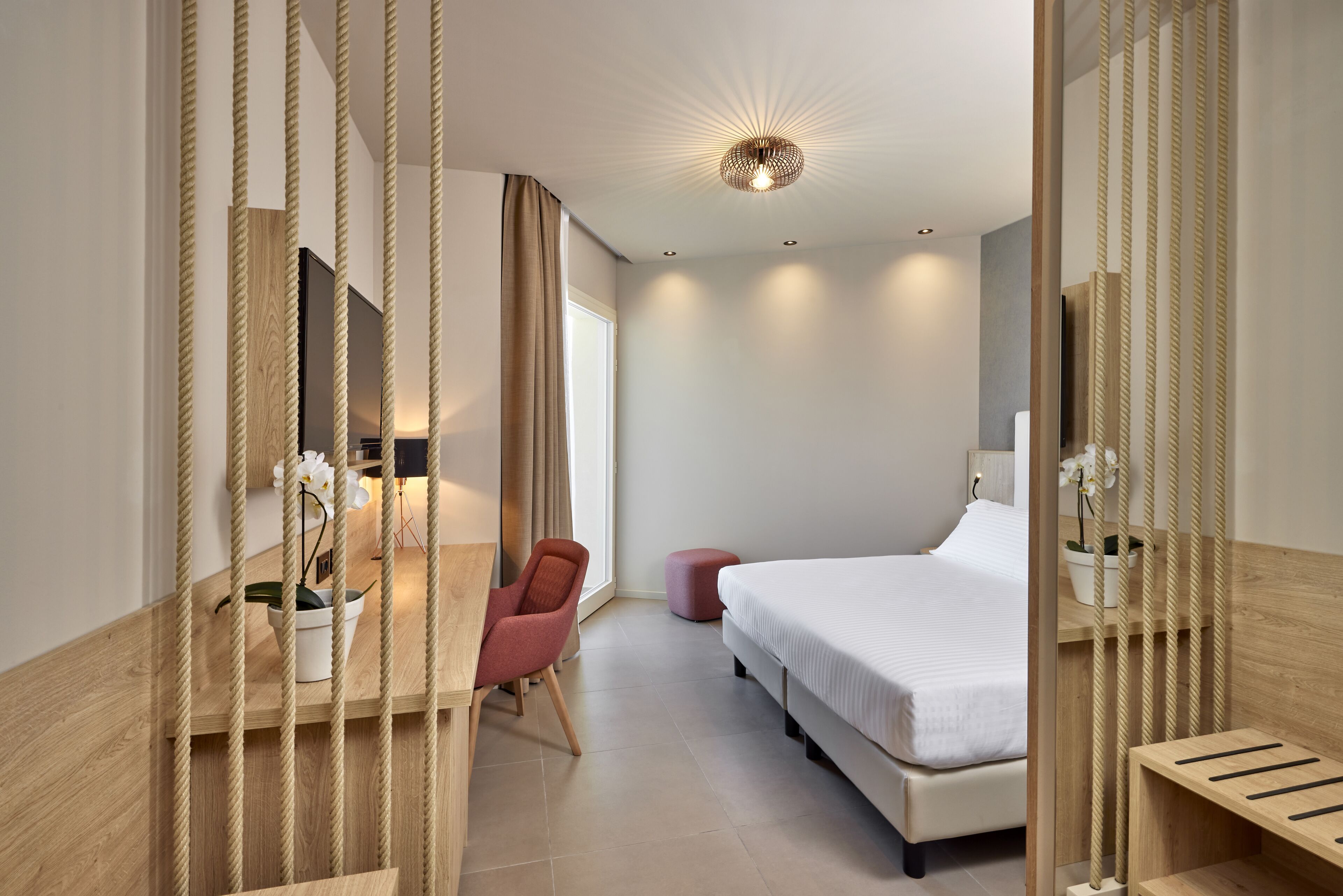 Ein modernes Hotelzimmer mit Bett, Schreibtisch, Stuhl und einer Zimmerpflanze.