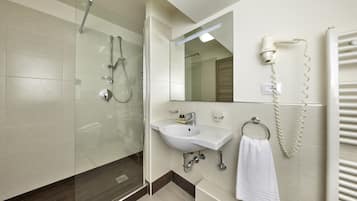 Un baño moderno con ducha de vidrio, lavamanos con argolla para toallas y secador de pelo montado en la pared.