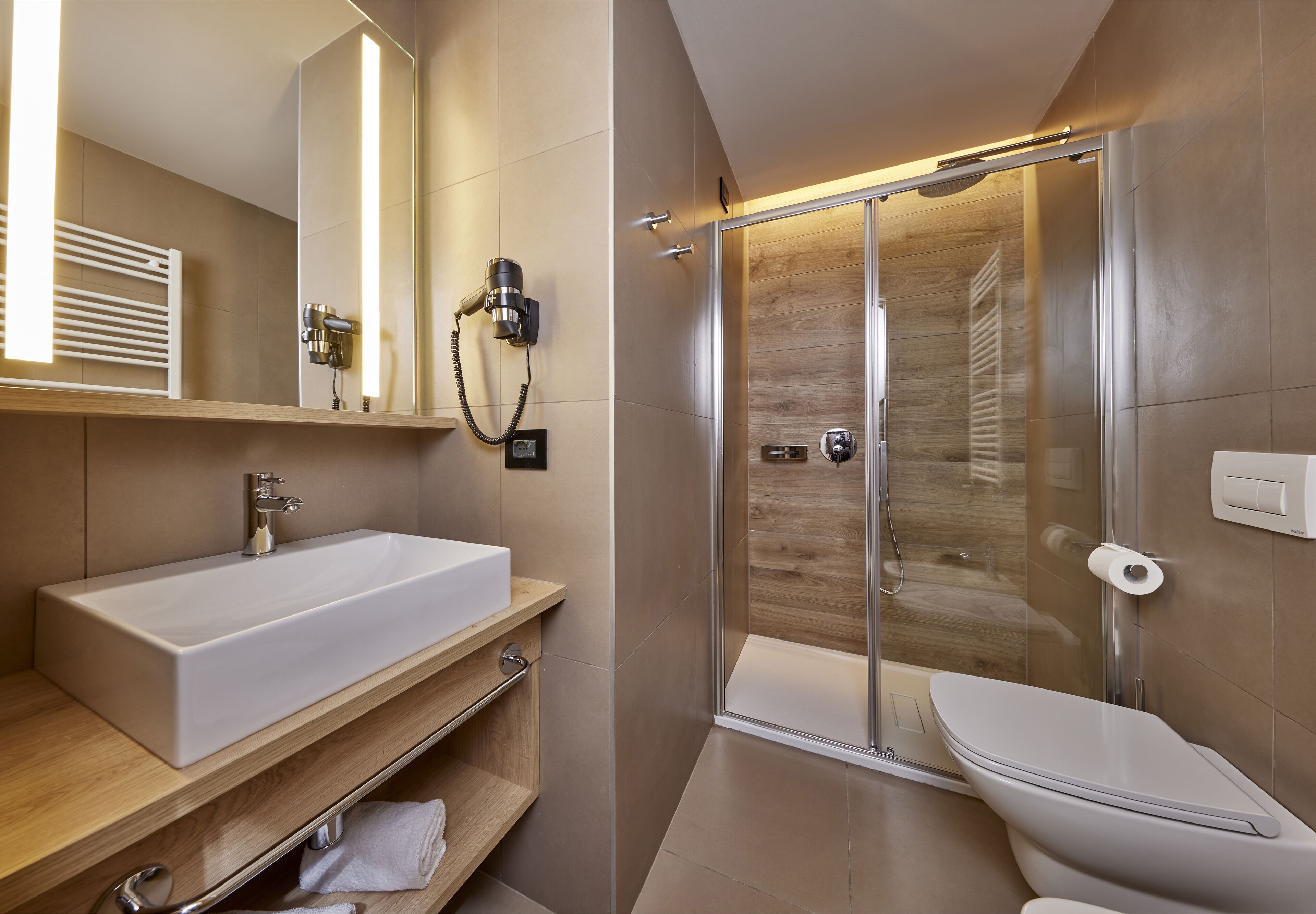 A modern bathroom with a large white sink, a glass-enclosed shower, and a toilet.