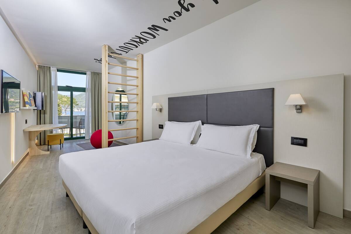 A modern hotel room with a large bed, a desk, and a view of the outdoors.