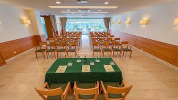 Ein Konferenzraum mit Reihen aus Holzwstühlen, einem grünen Tisch mit Namensschildern und Blick ins Freie durch große Fenster.