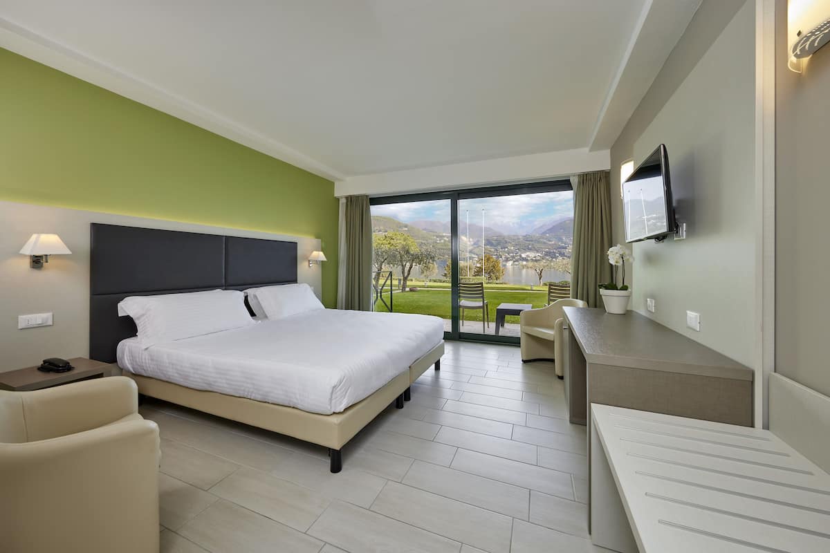 A hotel room with a bed, a desk, a chair, a TV, and a view of the outdoors.