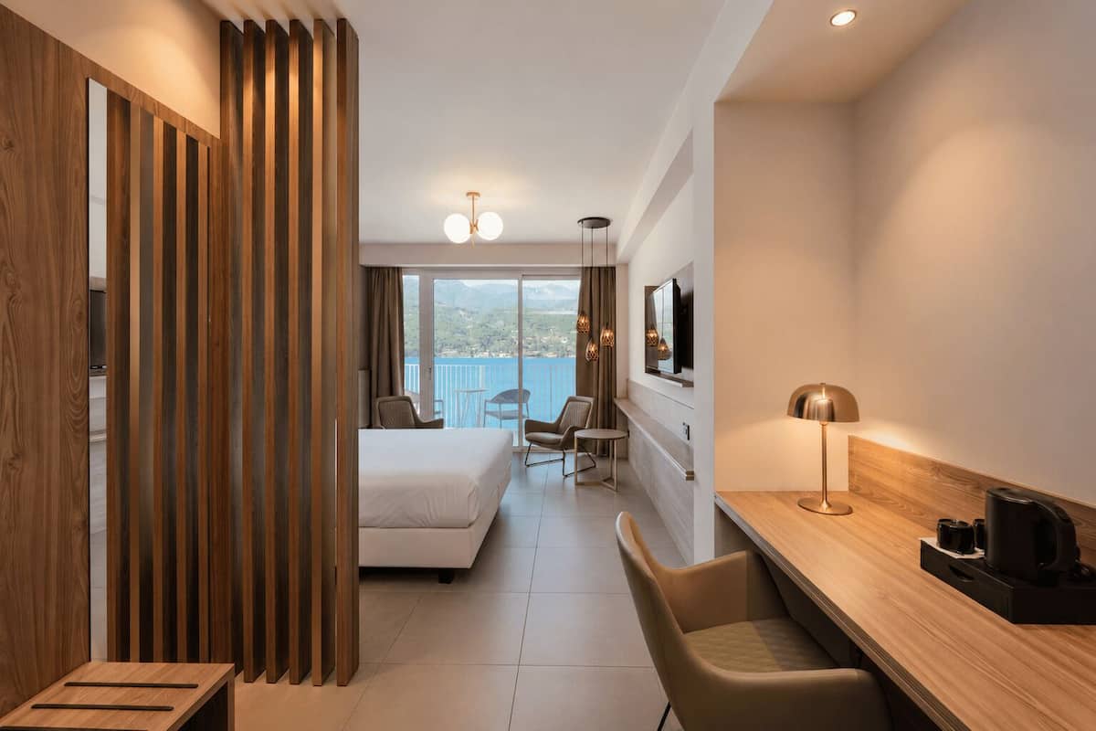 A modern hotel room with a bed, seating area, and a desk with a coffee maker.