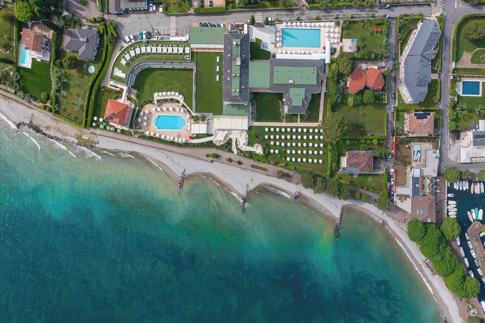 An aerial view of a coastal property with a swimming pool, tennis courts, and a marina.