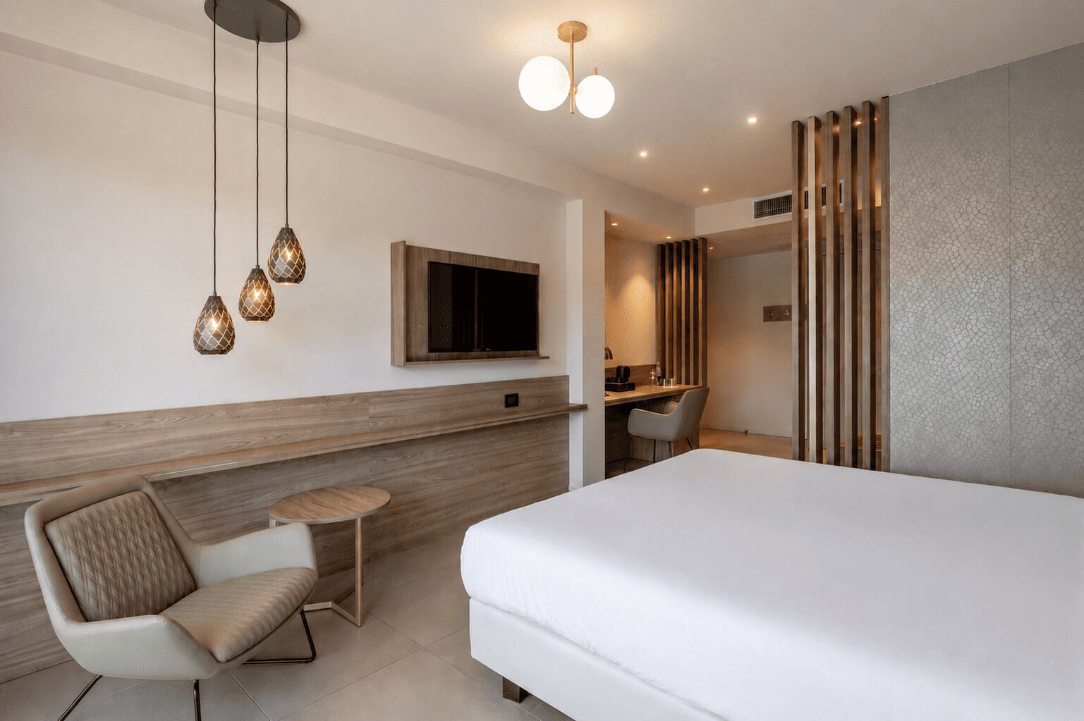 Ett modernt hotellrum med en stor säng, ett skrivbord, en stol, en TV och hängande lampor.