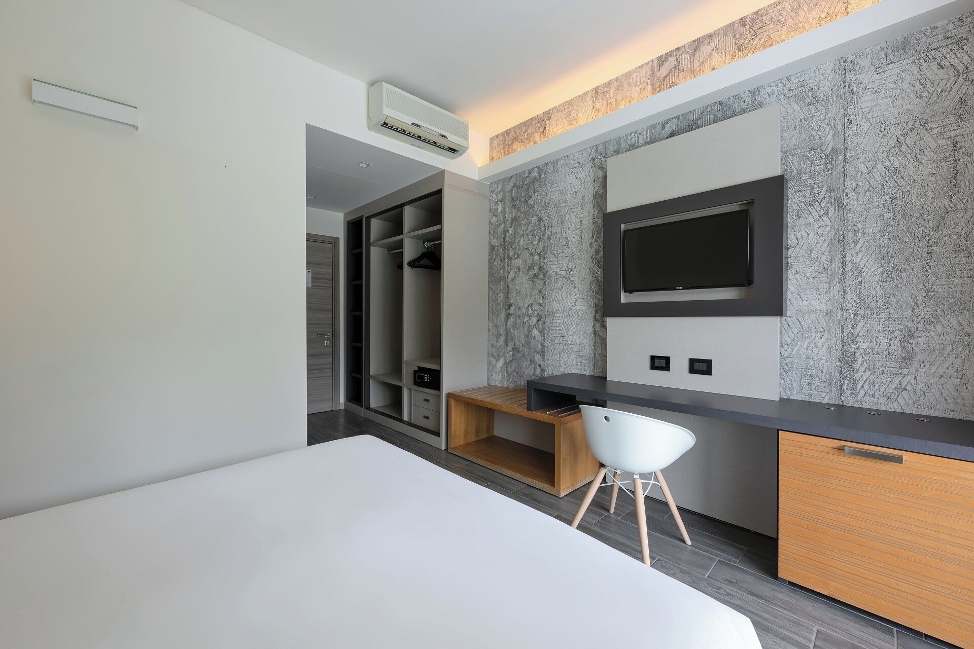 A modern hotel room with a bed, a desk, a TV, and a walk-in closet.