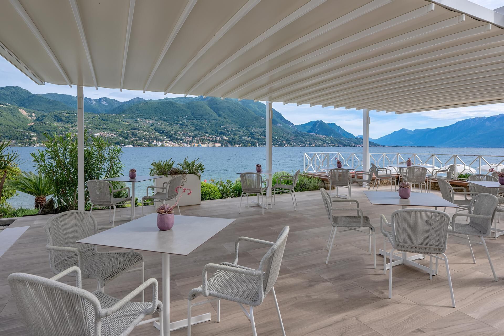 An outdoor patio with tables and chairs, overlooking a lake and mountains.