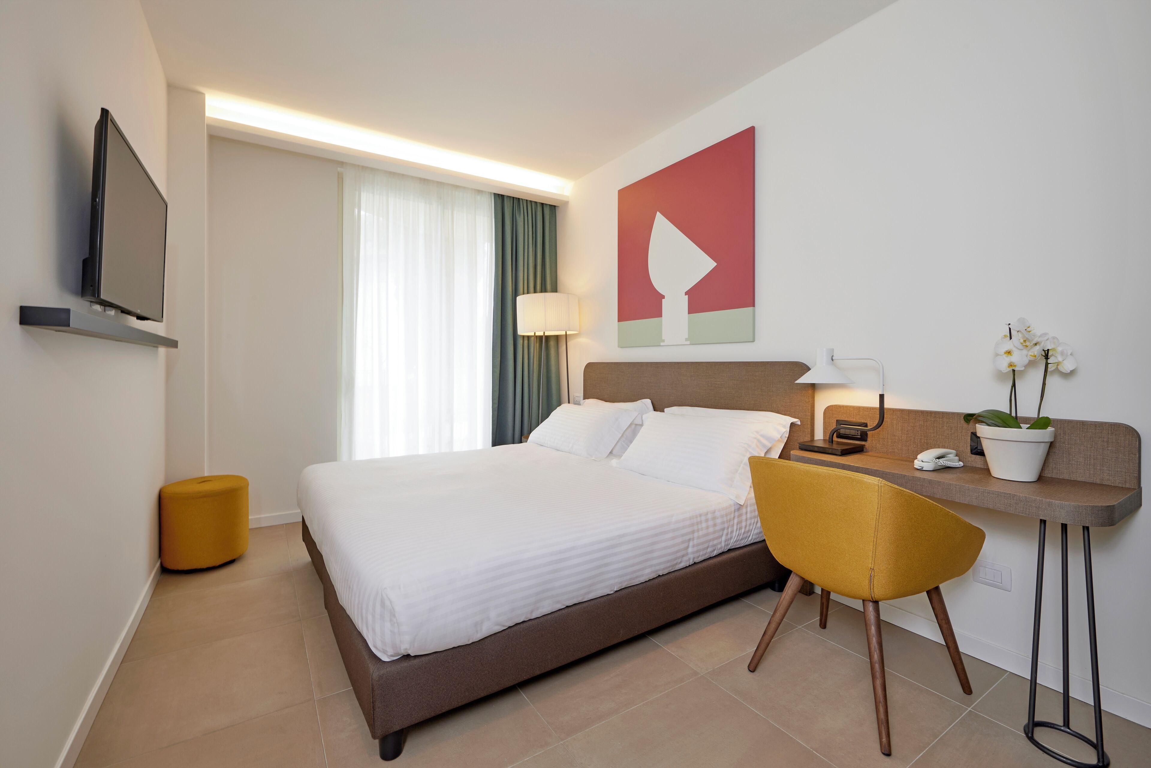 Una habitación de hotel moderna con una cama grande, un escritorio con una silla, un televisor, una lámpara y una planta en maceta.