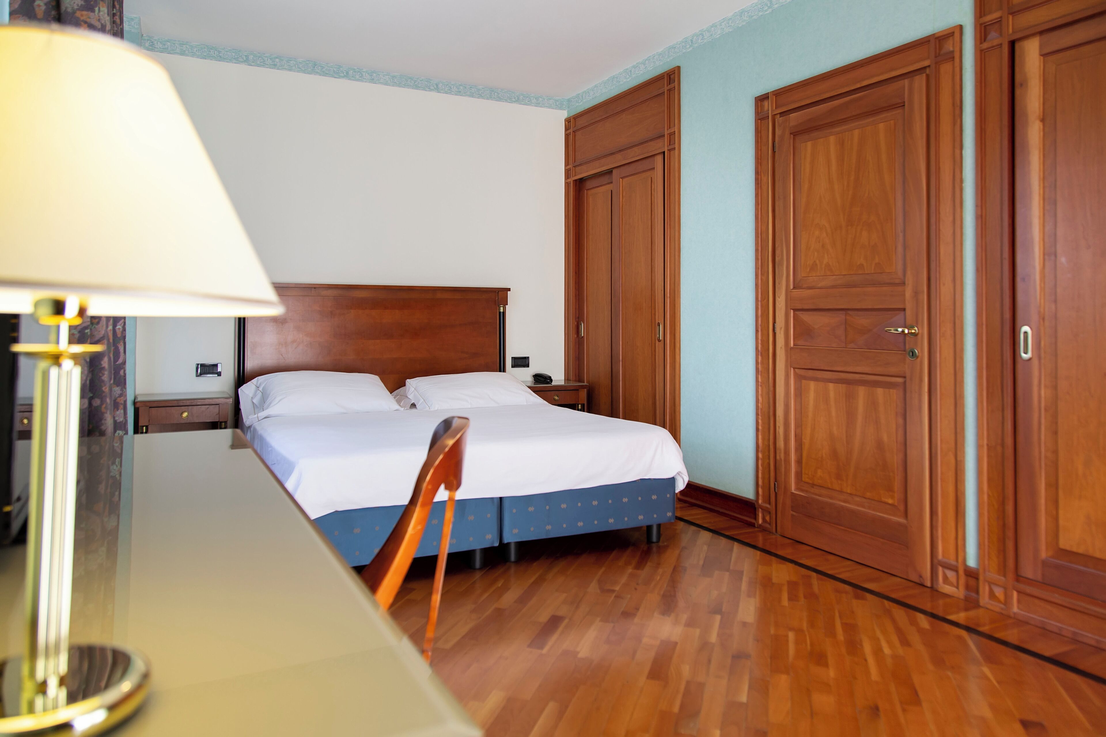 A hotel room with a wooden bed, a desk, and a lamp.