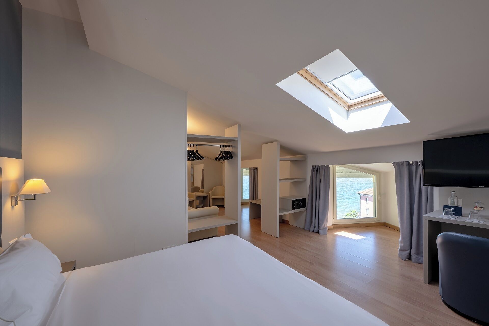 Ein Hotelzimmer mit Oberlichter, einem Bett, einem Schreibtisch, einem Sessel und Meerblick.
