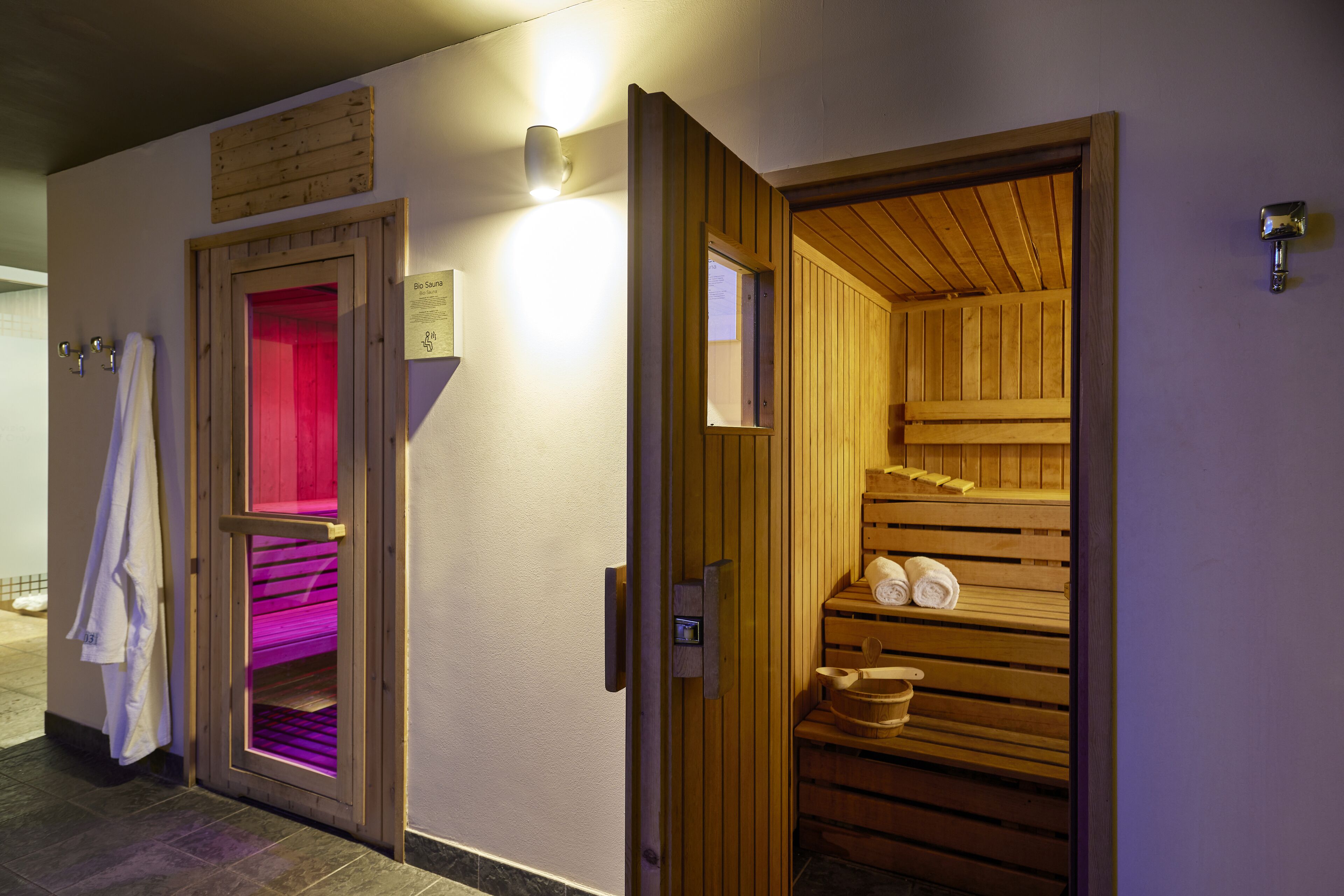 A sauna room with wooden benches and a red-lit steam room adjacent to it.