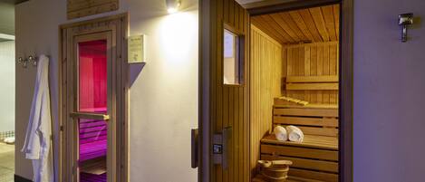 A sauna room with wooden benches and a red-lit steam room adjacent to it.
