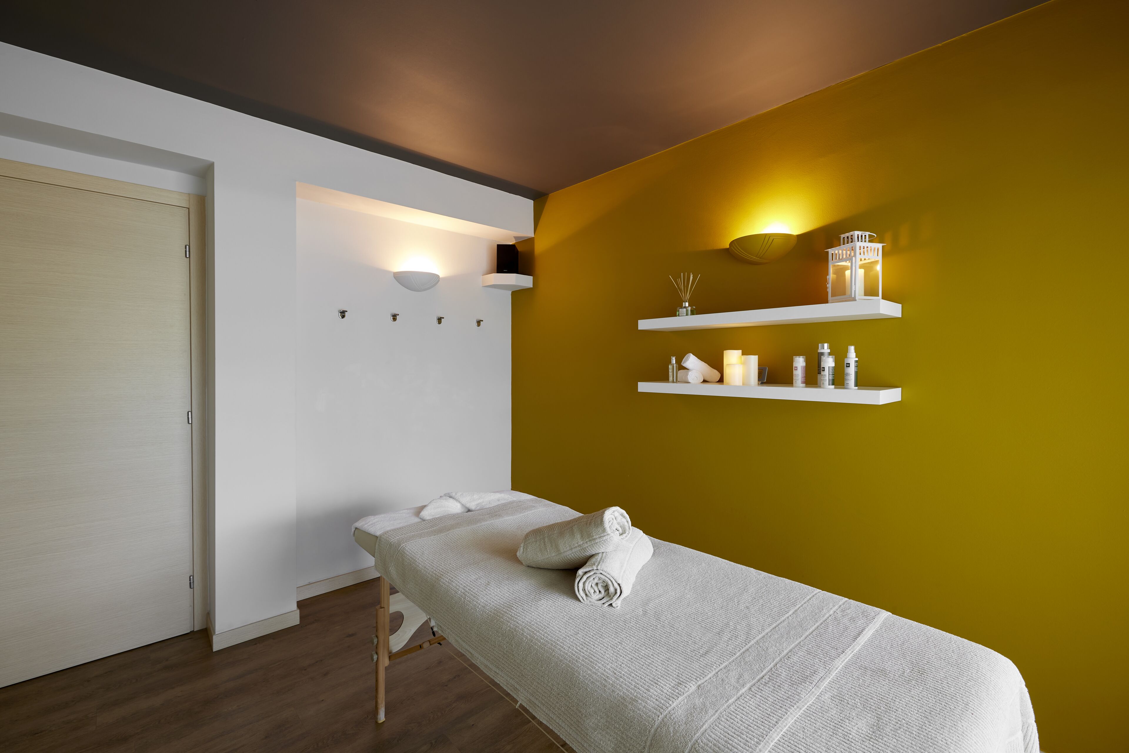 Una habitación con una camilla de masaje, una puerta blanca y una pared amarilla con estantes.