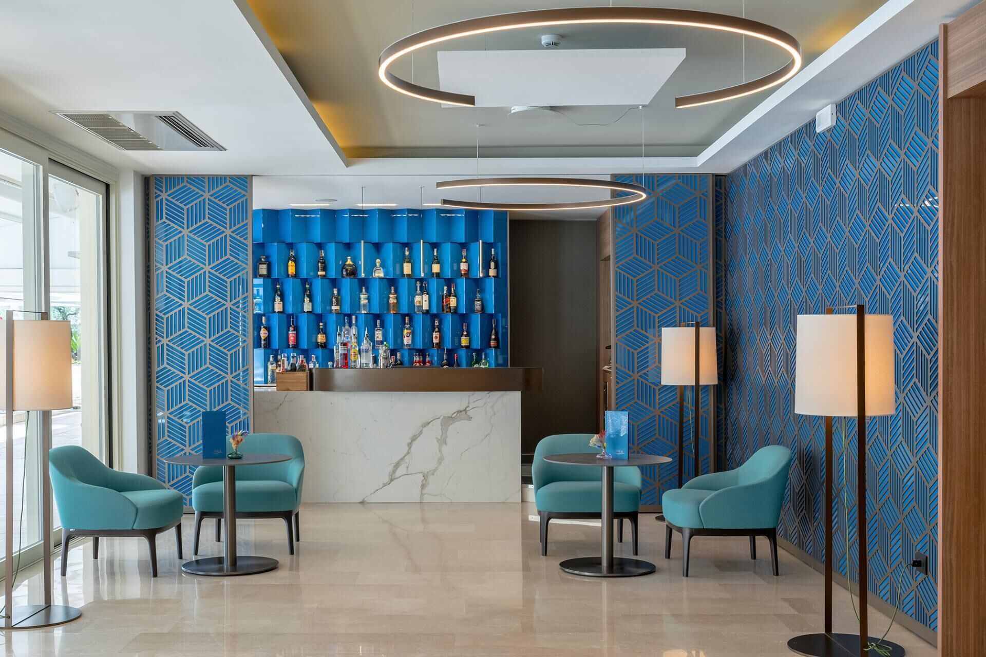 Zona de bar moderna con pared de diseño azulado, encimera de mármol y sillas color aguamarina.