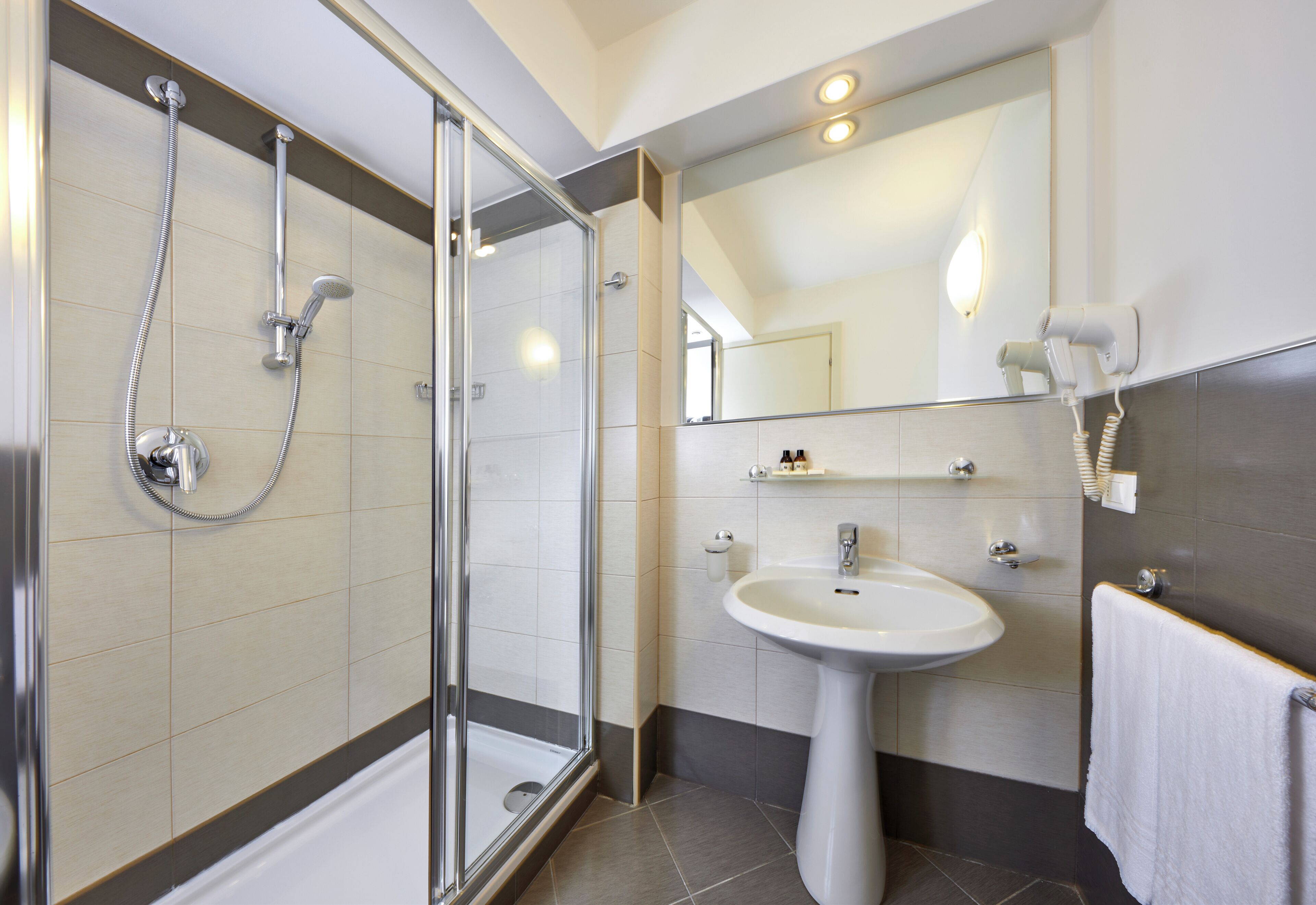 A modern bathroom with a glass shower enclosure, a pedestal sink, and a towel rack.