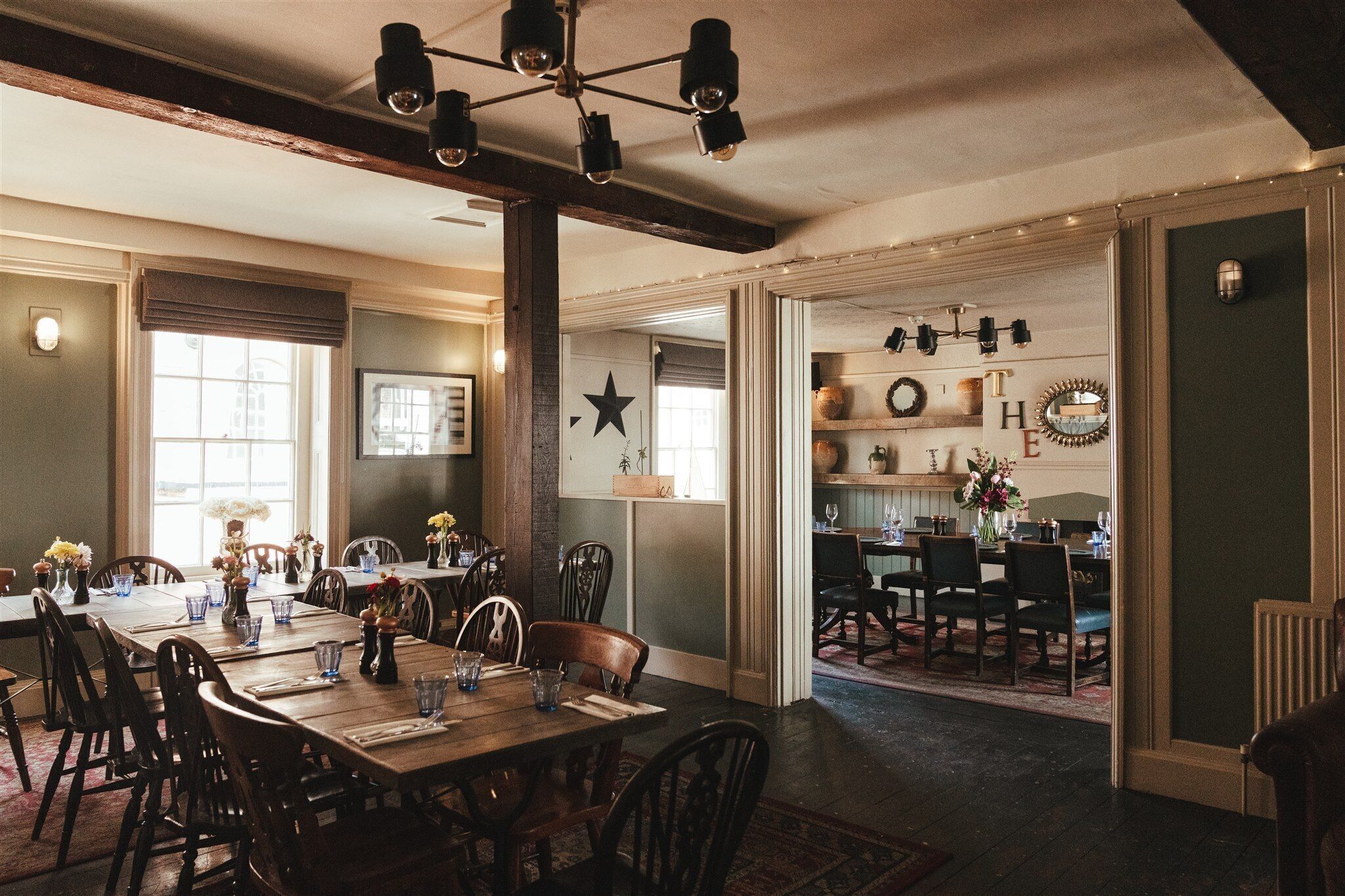 A dining area with wooden tables and chairs, a chandelier, and decorative wall elements.
