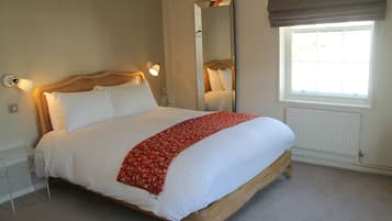 A neatly made bed with a red patterned throw, a bedside lamp, a mirror, and a window with a view of the outdoors.
