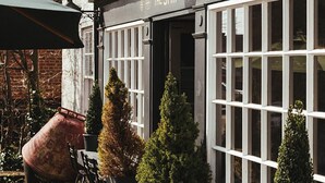 A traditional building with a sign reading "The Ship Inn". It features large windows, outdoor seating with tables and chairs, and decorative potted plants. - The Ship Inn (Rye)