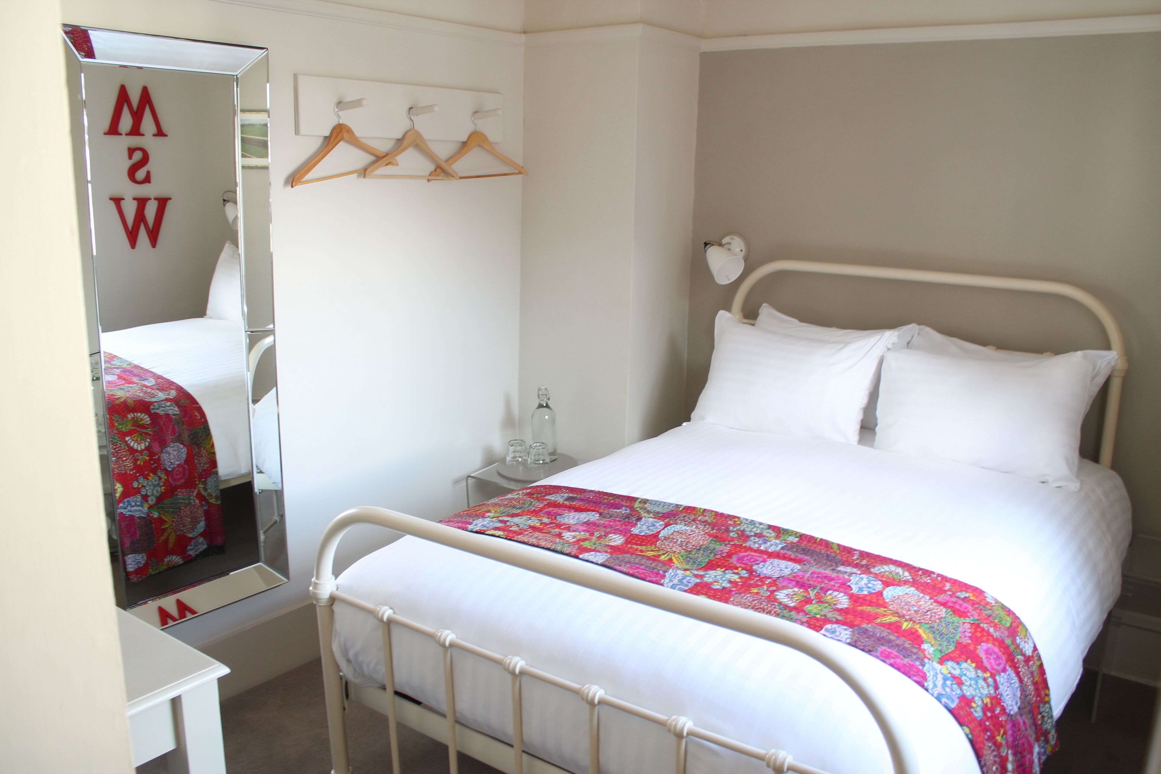 A bedroom with a bed, a bedside table, a mirror, and a wardrobe.