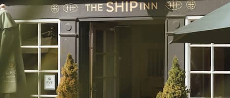 The exterior of The Ship Inn, featuring a traditional black and white facade, a welcoming entrance, and two potted evergreen plants at the doorway.