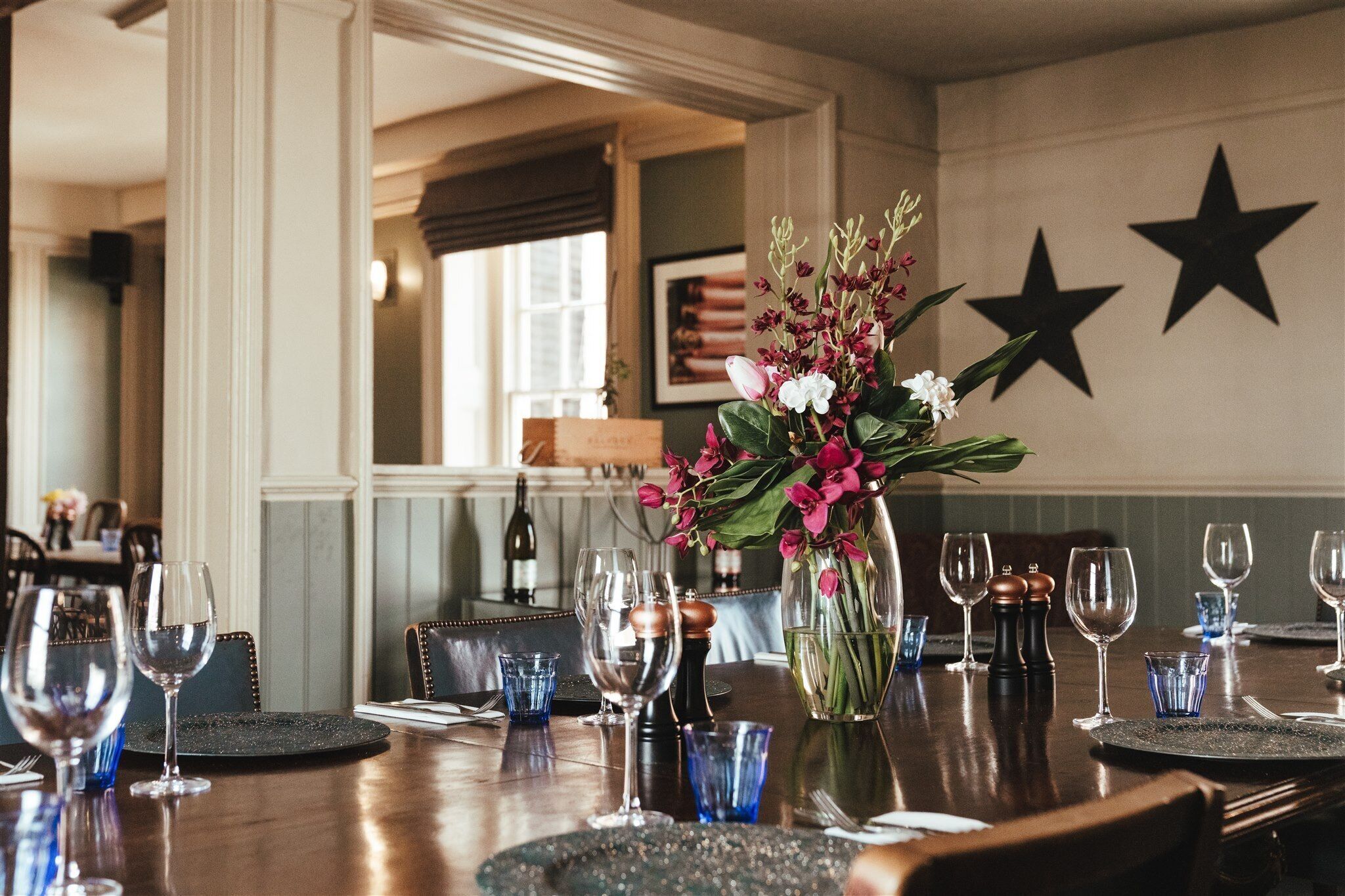 Une table à manger dressée avec des verres à vin, des verres à eau bleus et un vase rempli de fleurs.