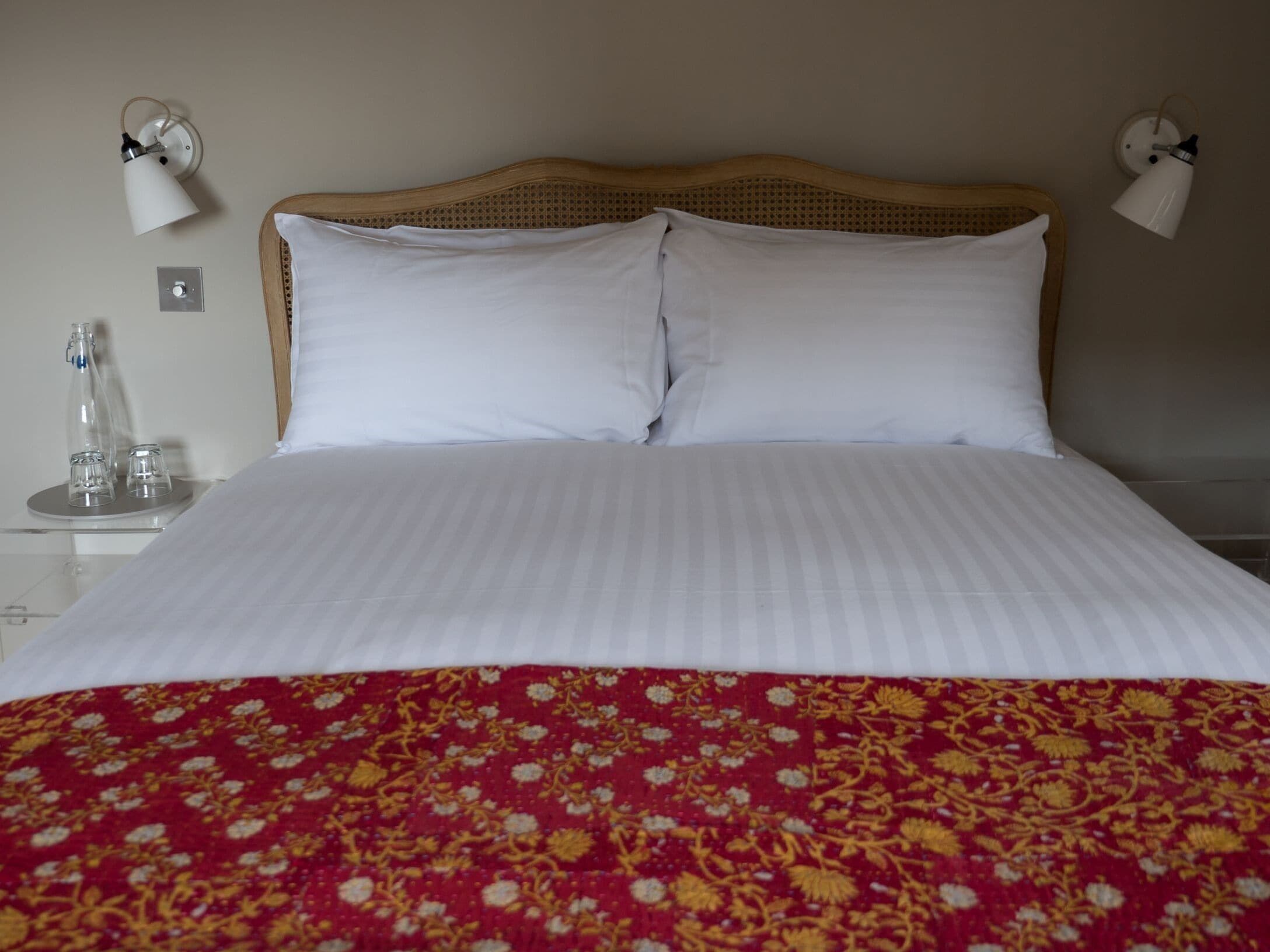 A neatly made bed with white linens and a red floral bedspread. There are two bedside lamps on either side of the bed.