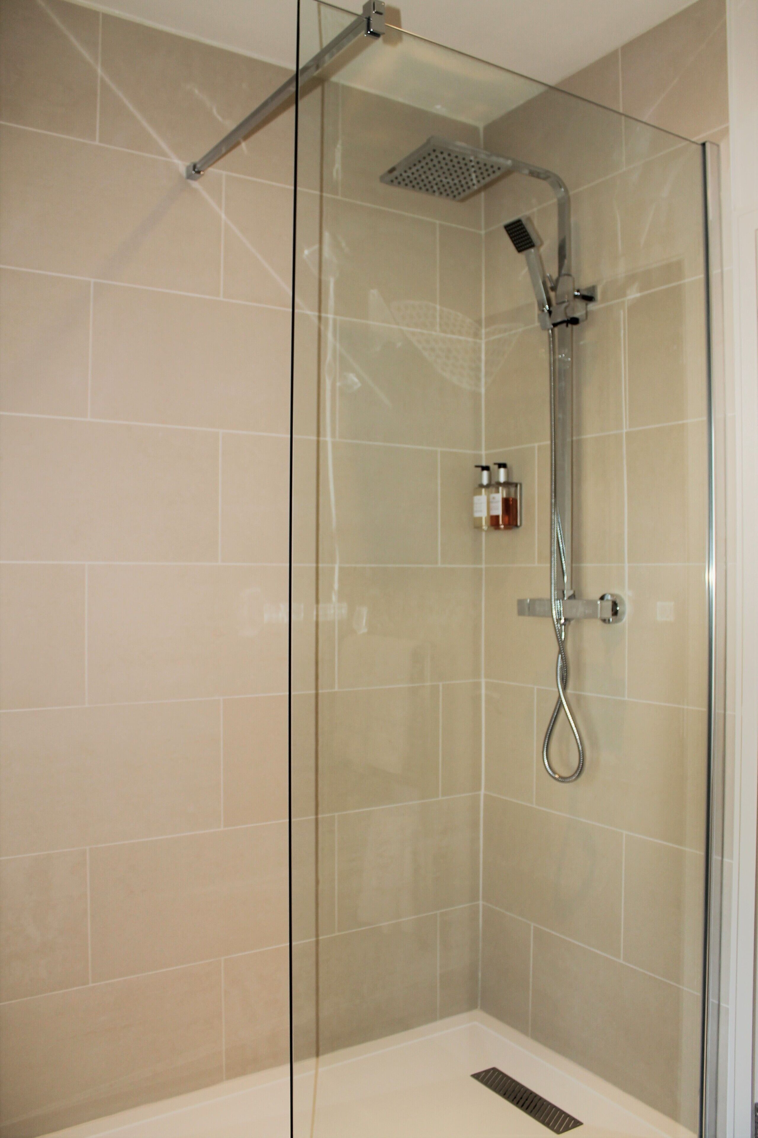 A glass-enclosed shower with a handheld showerhead and a wall-mounted control panel.