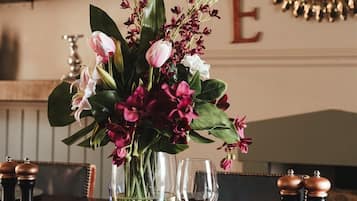 Una mesa de comedor dispuesta con un jarrón de flores, saleros y pimenteros, y una copa de vino.