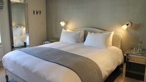A neatly made bed with white linens and a gray throw blanket, a bedside table with a lamp, and a mirror on the wall. - The Ship Inn (Rye)