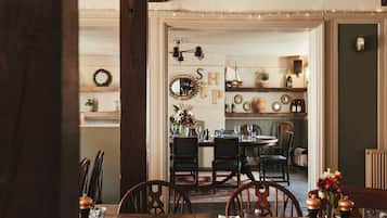 A dining area with wooden tables and chairs, a chandelier, and a wall with decorative items and a sign.