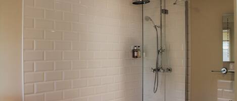 Un baño moderno con azulejos blancos tipo metro, una ducha con cerramiento de vidrio, una bañera blanca y un lavamanos con espejo.