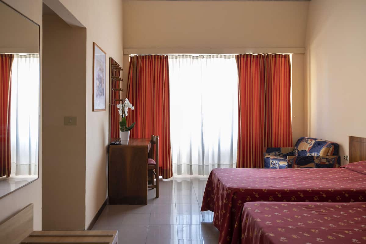Une chambre d’hôtel avec deux lits, un bureau, une chaise et une plante en pot.