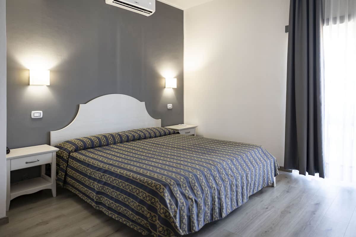 Une chambre à coucher avec un lit, des tables de chevet, des lampes fixées au mur et une fenêtre avec des rideaux.