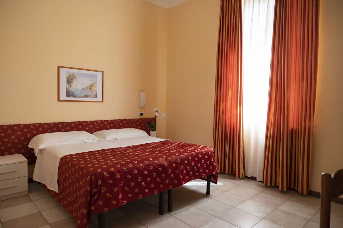 Une chambre d’hôtel avec un lit, une table de chevet, un tableau encadré au mur et une fenêtre avec des rideaux.