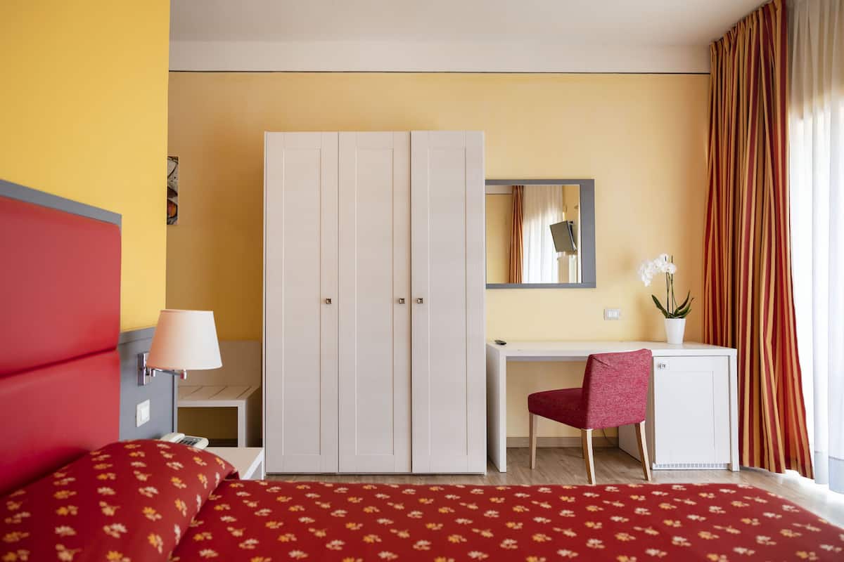 Une chambre d’hôtel comprenant un lit, un bureau, une armoire, une chaise, une lampe et une plante en pot.