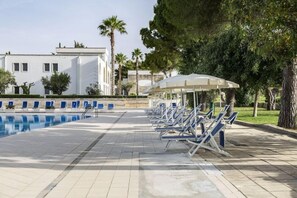 Una piscina al aire libre, sombrillas, sillones reclinables de piscina
