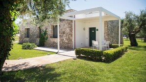 A stone building with a covered patio area, a door, and a small seating area with chairs. - Color Dolmen Family Village (Minervino di Lecce)