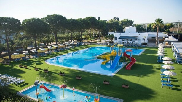 A swimming pool with slides and water play area, surrounded by lounge chairs and umbrellas. - Color Dolmen Family Village (Minervino di Lecce)