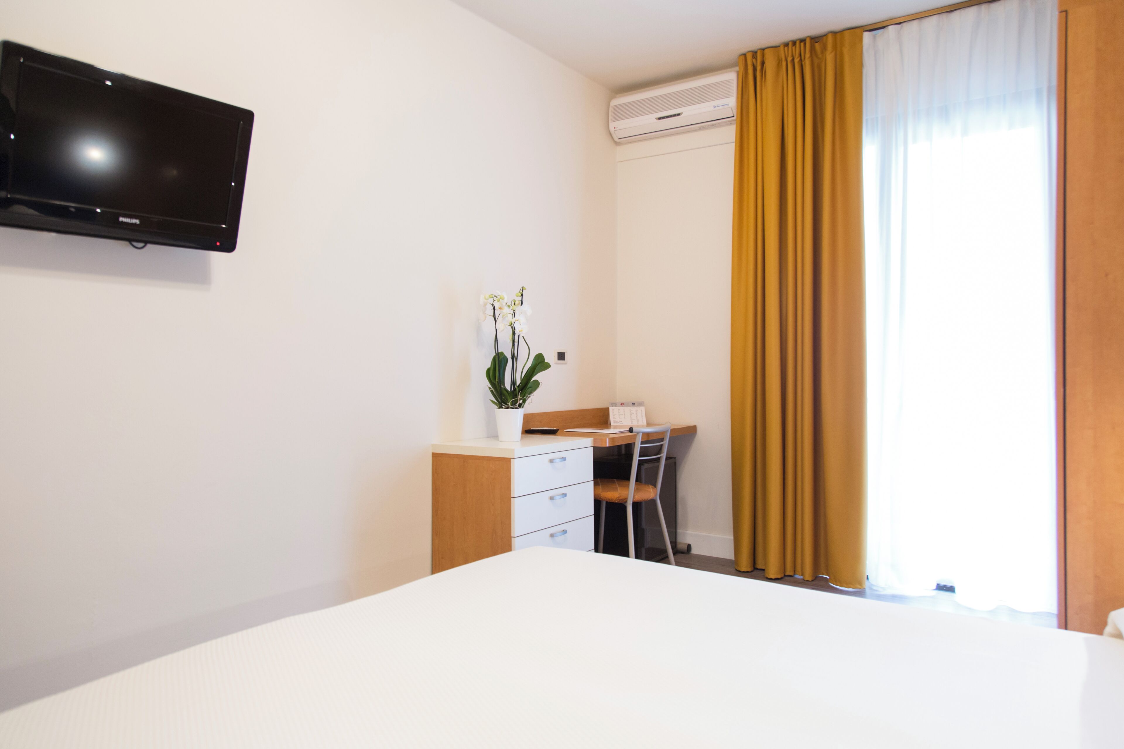Ein Hotelzimmer mit Bett, Schreibtisch mit Stuhl, Wandfernseher und einem Fenster mit Vorhängen.