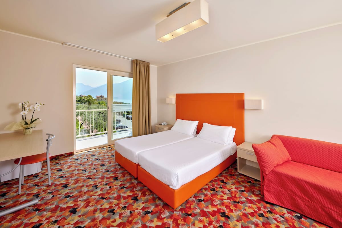Une chambre d’hôtel avec un grand lit, un bureau, un canapé rouge et une vue sur l’extérieur.